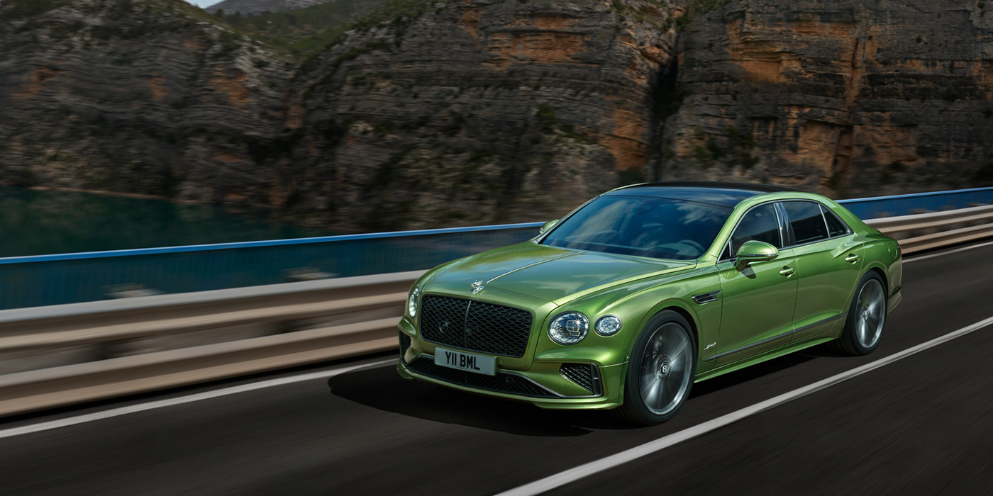 Bentley Bristol Bentley New Flying Spur Speed v8 hybrid sedan driving dynamically on a mountain road in Tourmaline Green paint