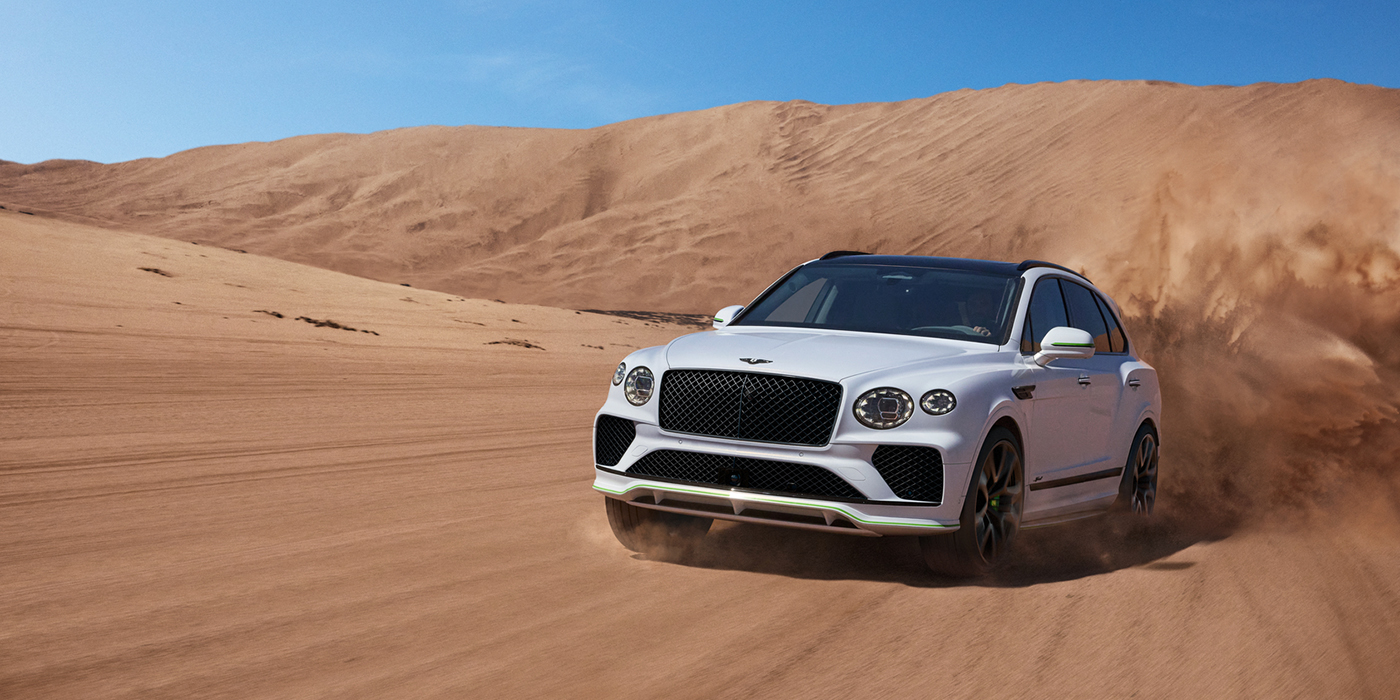 Bentley Bristol Bentley Bentayga Speed SUV front three quarter in Snow Quarts Pearlescent by Mulliner white paint driving dynamically through the desert