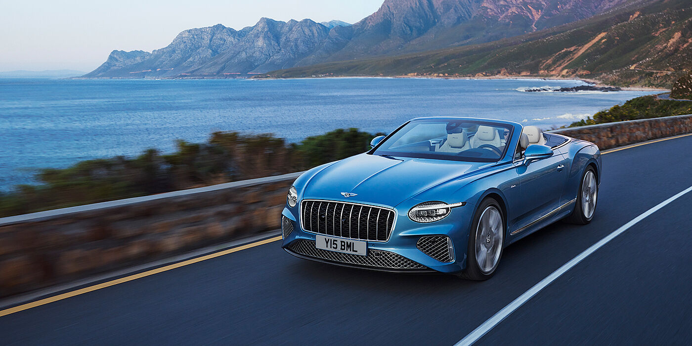 Bentley Bristol New Bentley Continental GTC Azure convertible in Light Windsor blue paint with 22 inch Azure wheels and chrome grill, driving dynamically by the sea