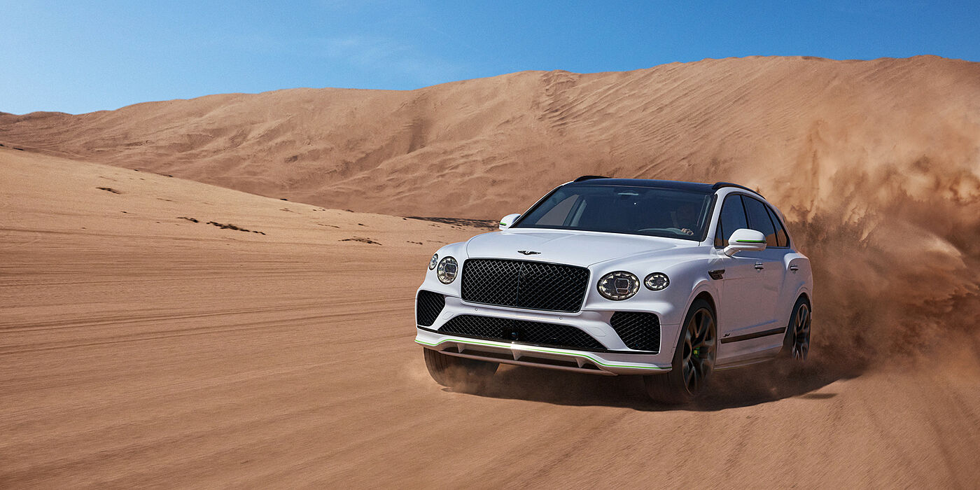 Bentley Bristol Bentley Bentayga Speed SUV front three quarter in Snow Quarts Pearlescent by Mulliner white paint driving dynamically through the desert