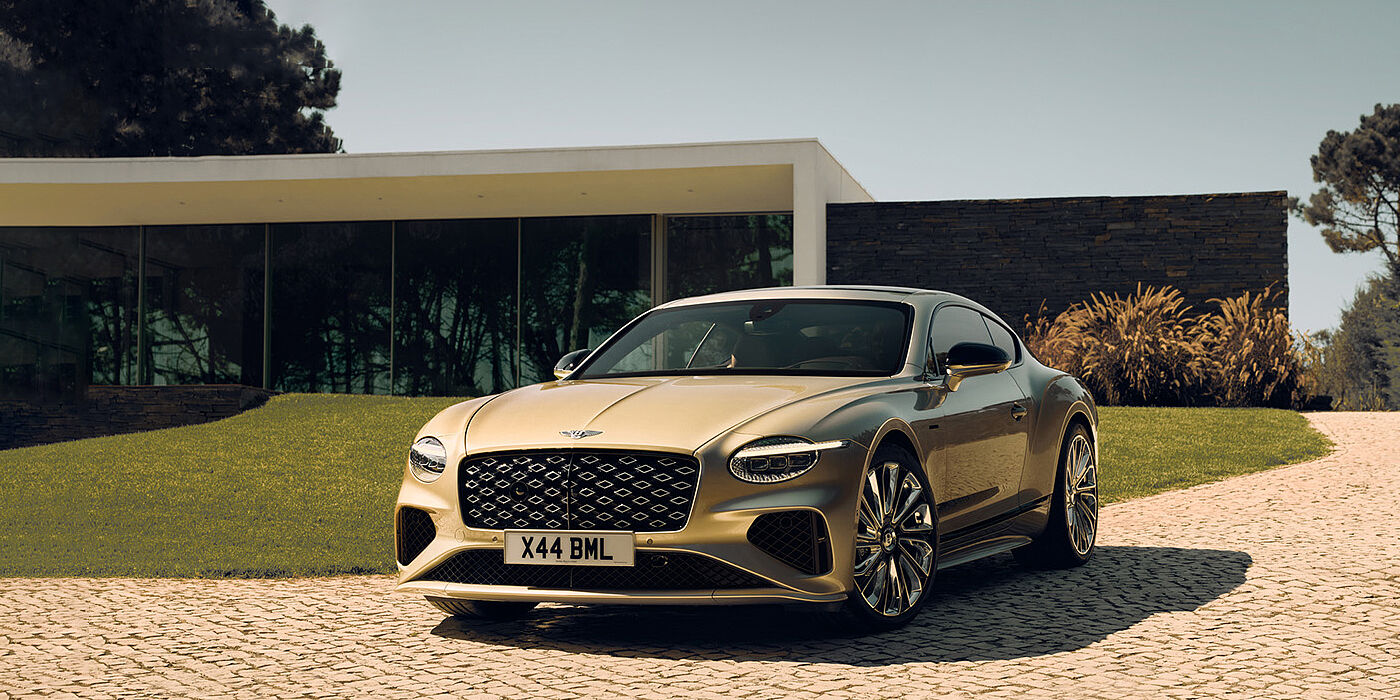 Bentley Bristol Bentley Continental GT Mulliner coupe front three quarters in Patina paint parked outside a glass fronted building with a grass lawn behind it