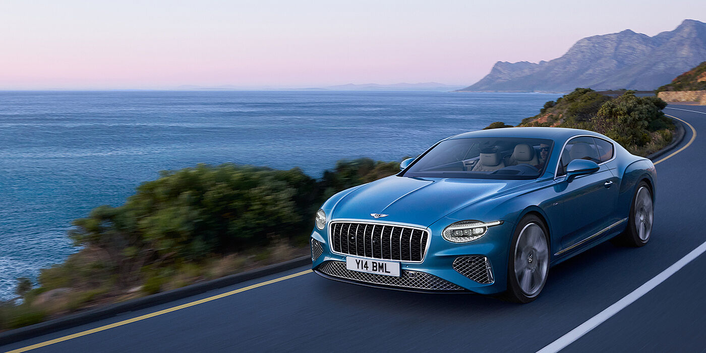 Bentley Bristol New Bentley Continental GT Azure coupe in Light Windsor blue paint with 22 inch Azure wheels and chrome grill, driving dynamically by the sea