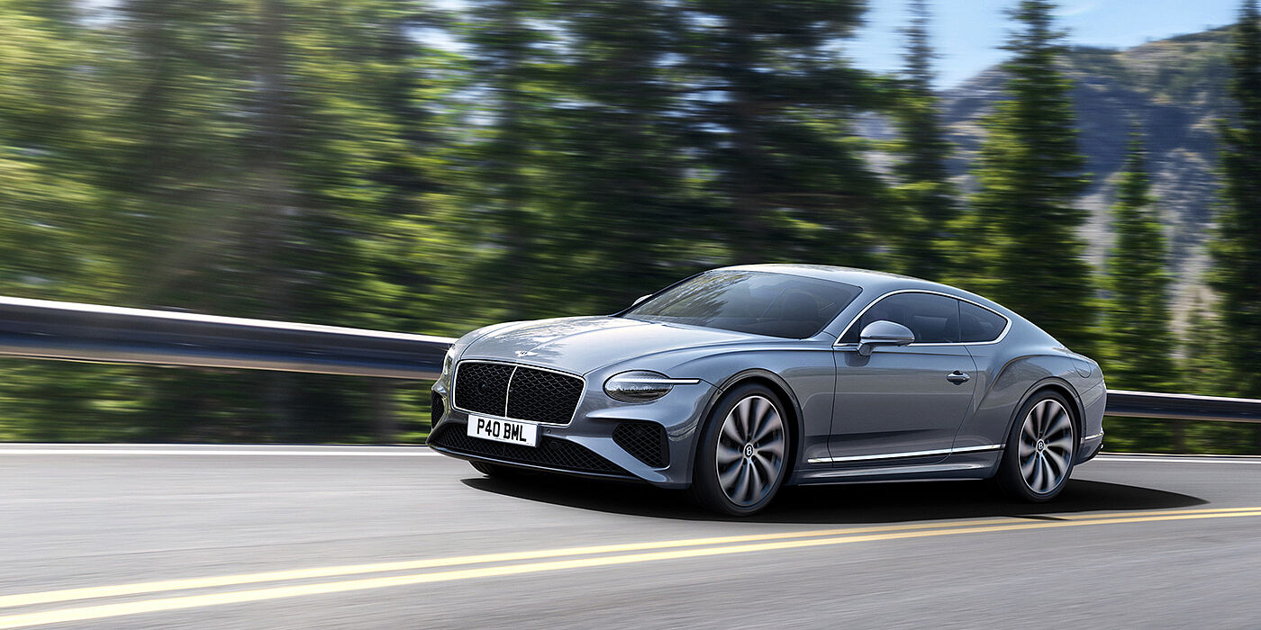 Bentley Bristol New Bentley Continental GT coupe in Silverlake paint and 22 inch ten-spoke wheels, driving dynamically on a tree-lined road in the sunshine