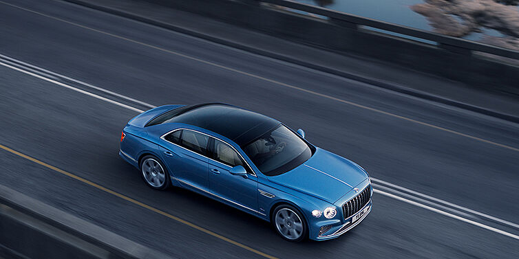 Bentley Bristol New Bentley Flying Spur Azure sedan in Light windsor blue paint by Mulliner, with 22 inch Azure wheels seen from overhead driving dynamically on a country road
