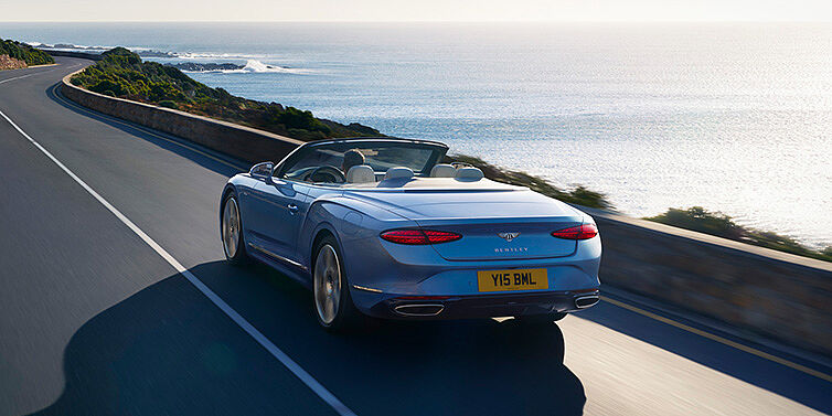 Bentley Bristol New Bentley Continental GTC Azure convertible rear view in Light Windsor blue paint with 22 inch ten spoke wheels driving dynamically on an ocean road in the sunshine