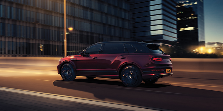 Bentley Bristol Bentley Bentayga Extended Wheelbase Mulliner SUV in Cricket Ball red paint driving dynamically in city at night